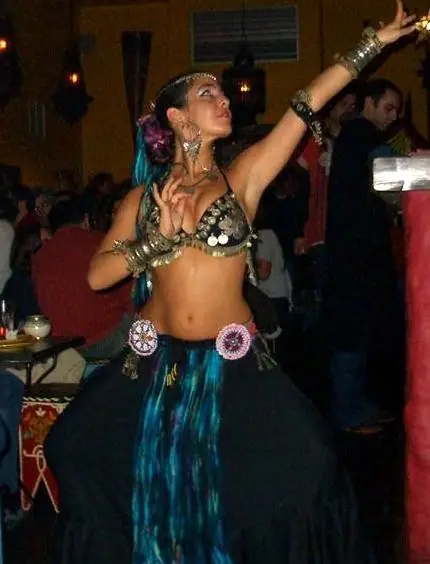 Ana in a black tribal-style costume with a coin bra, one arm raised