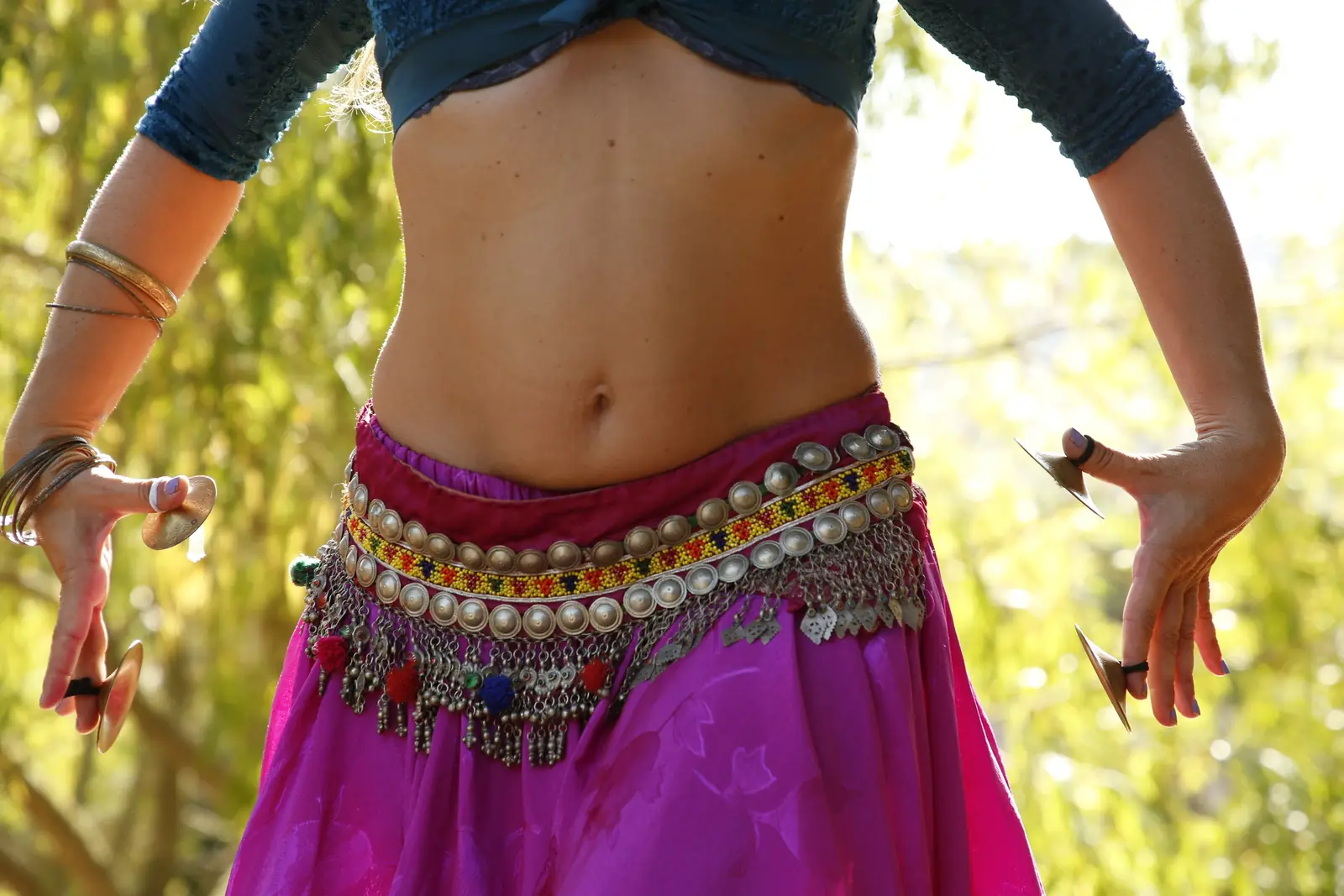 Close-up of a belly dance coin belt and fuchsia skirt, with finger cymbals on both hands