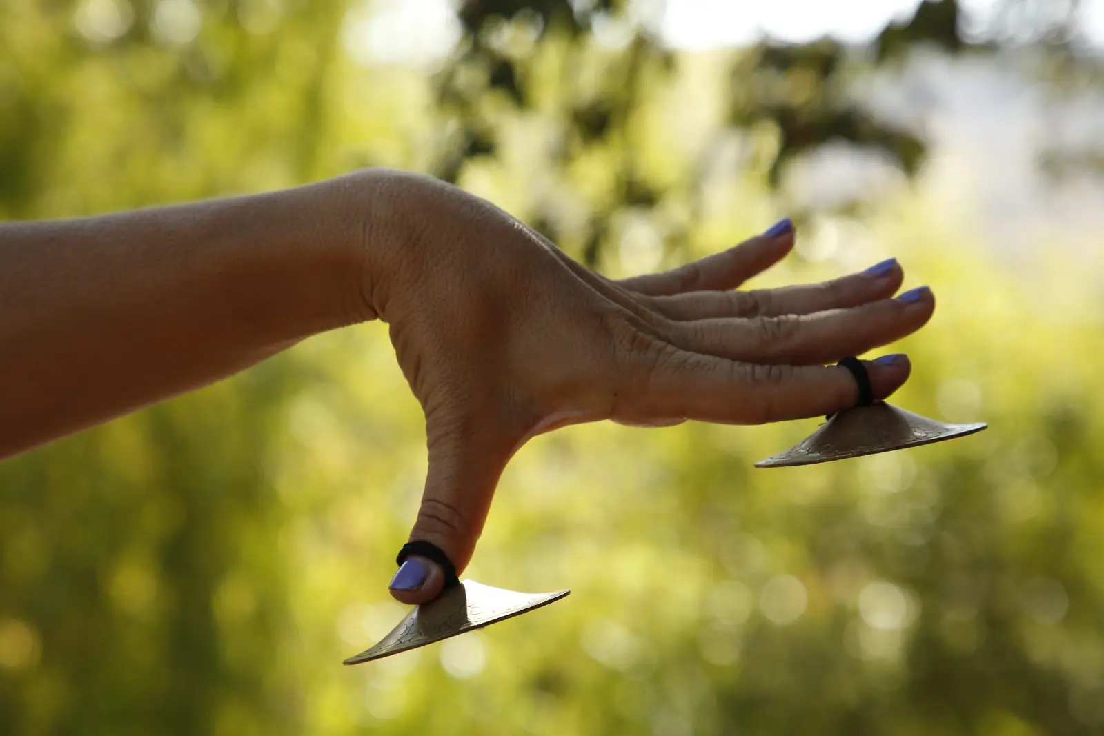 A dancer's hand with gold finger cymbals against a soft green background