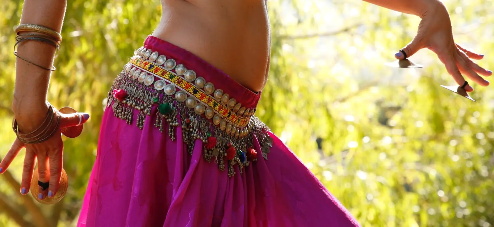 Close-up of a hip with a coin belt and a fuchsia skirt, and finger cymbals