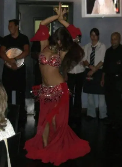 Ana in a red costume with her arms raised, a drummer behind her