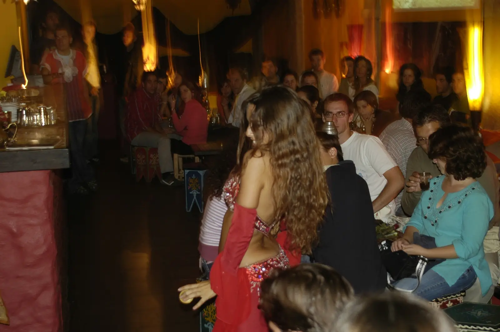Ana seen from behind in a red costume, dancing among the seated audience