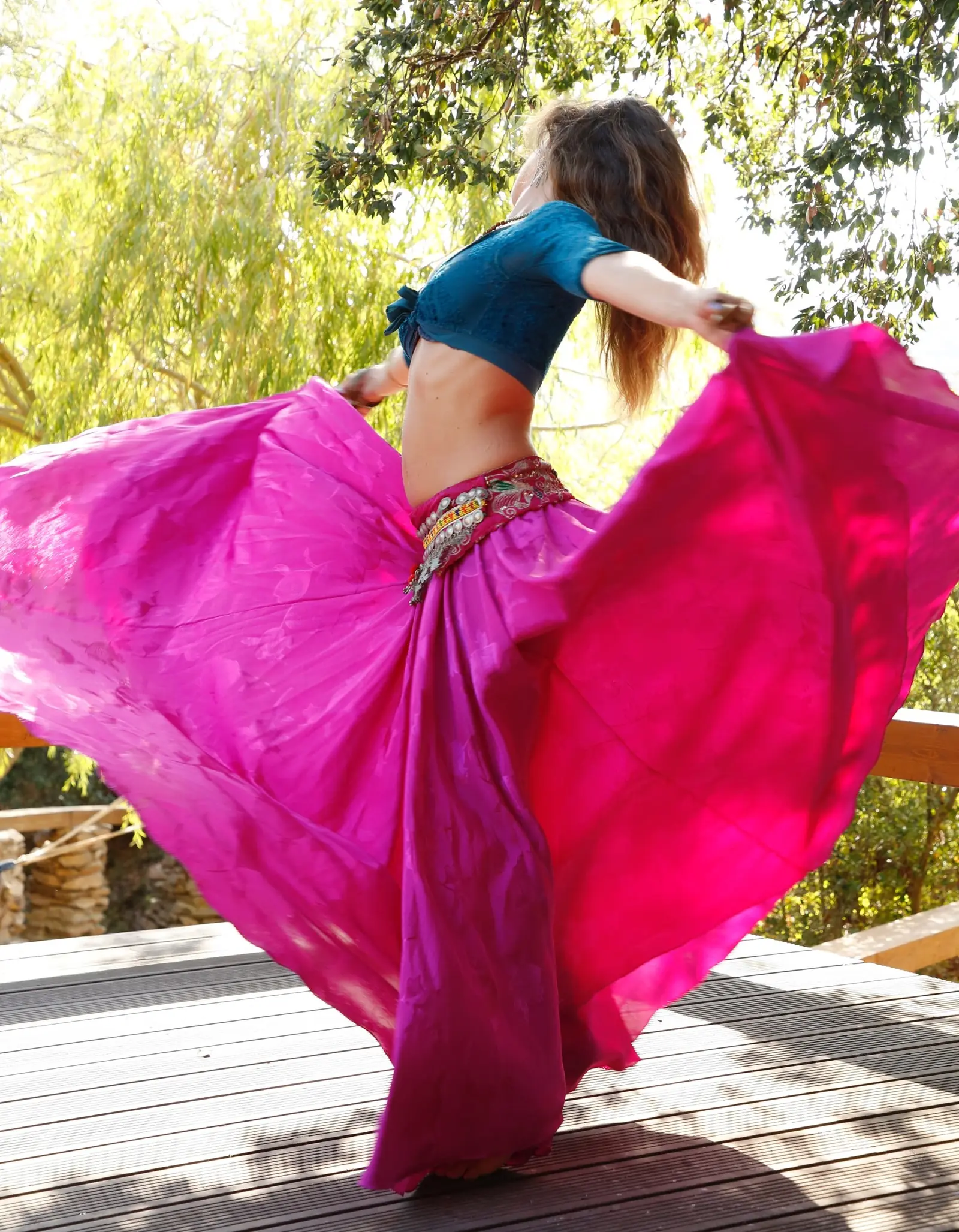 Ana spinning with her fuchsia skirt fanned out on a wooden deck, among trees