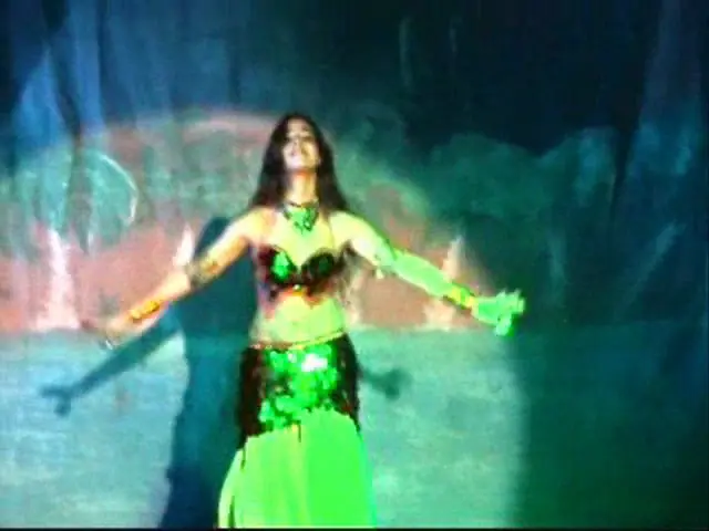Ana on stage under green light, arms open