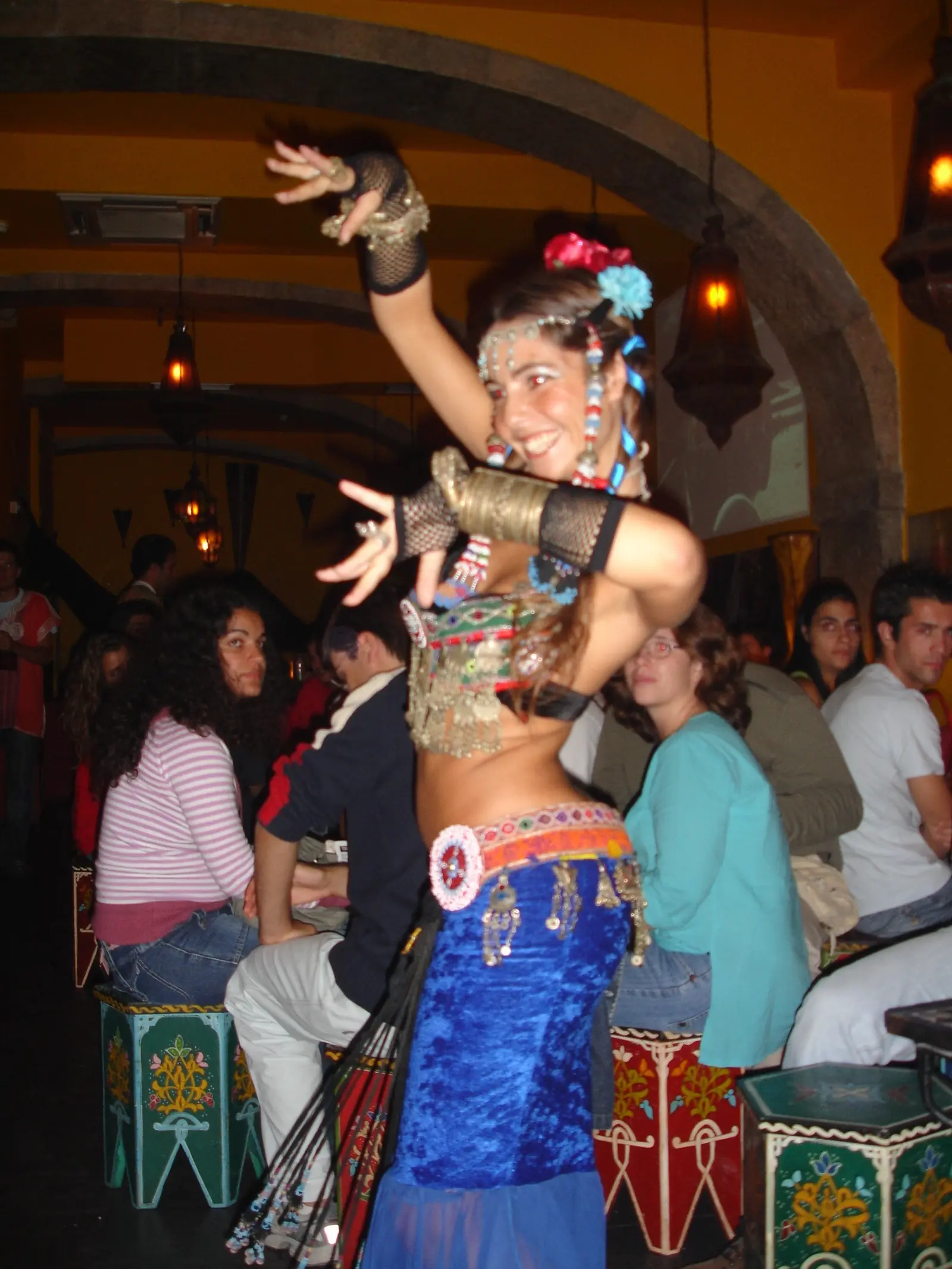 Ana smiling in a tribal-style costume with flowers and a coin belt, in a Moroccan-style restaurant