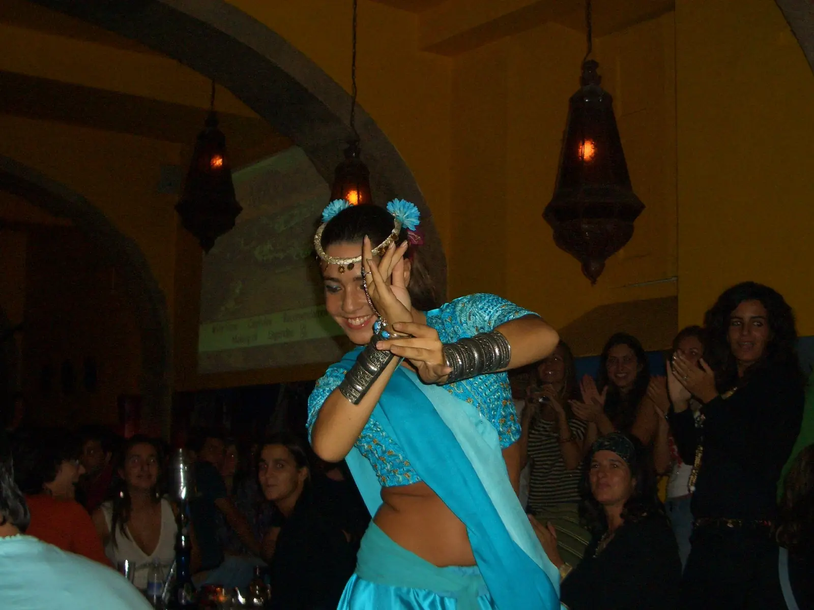 Ana in a turquoise costume with flowers in her hair, dancing among the audience