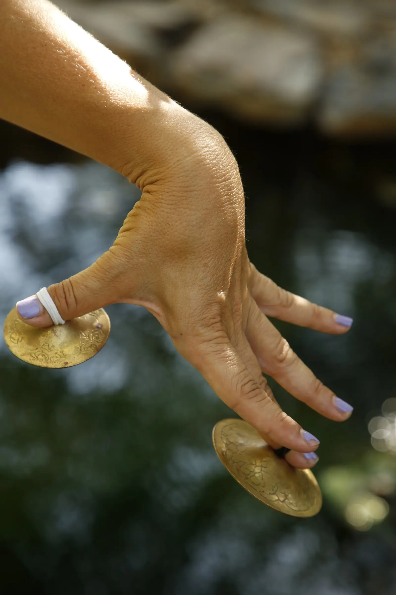 A hand with gold finger cymbals over dark water